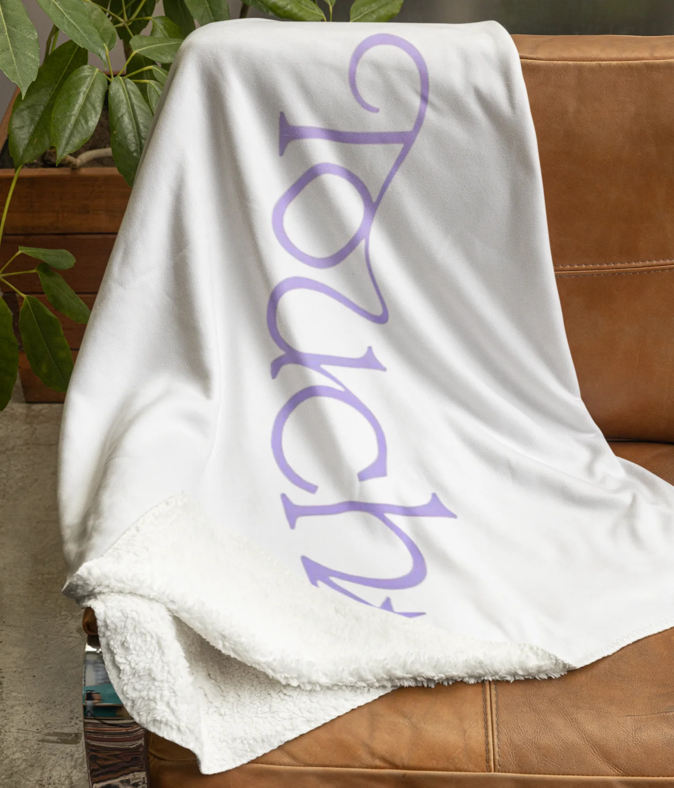 white katseye blanket with touch purple design on a luxurious couch next to a plant